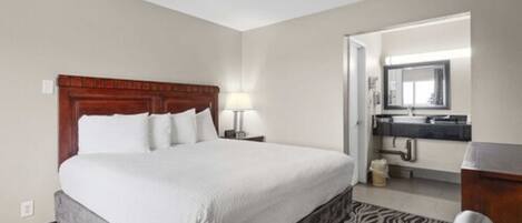 Une chambre d’hôtel avec un grand lit, une tête de lit en bois, une table de chevet avec une lampe, un tapis à motifs zébrés et une salle de bain avec un miroir et un lavabo.