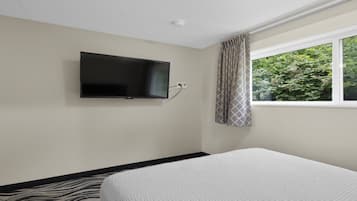 Une chambre d’hôtel avec un lit, un téléviseur fixé au mur et une fenêtre avec des rideaux.