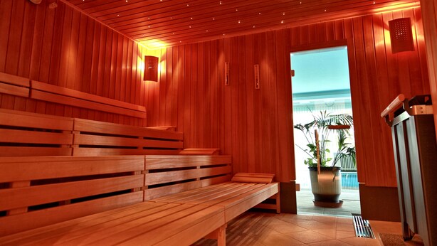 A wooden sauna with benches, a clock, and a view of the ocean. - Top Hotel Agricola (Marianske Lazne)