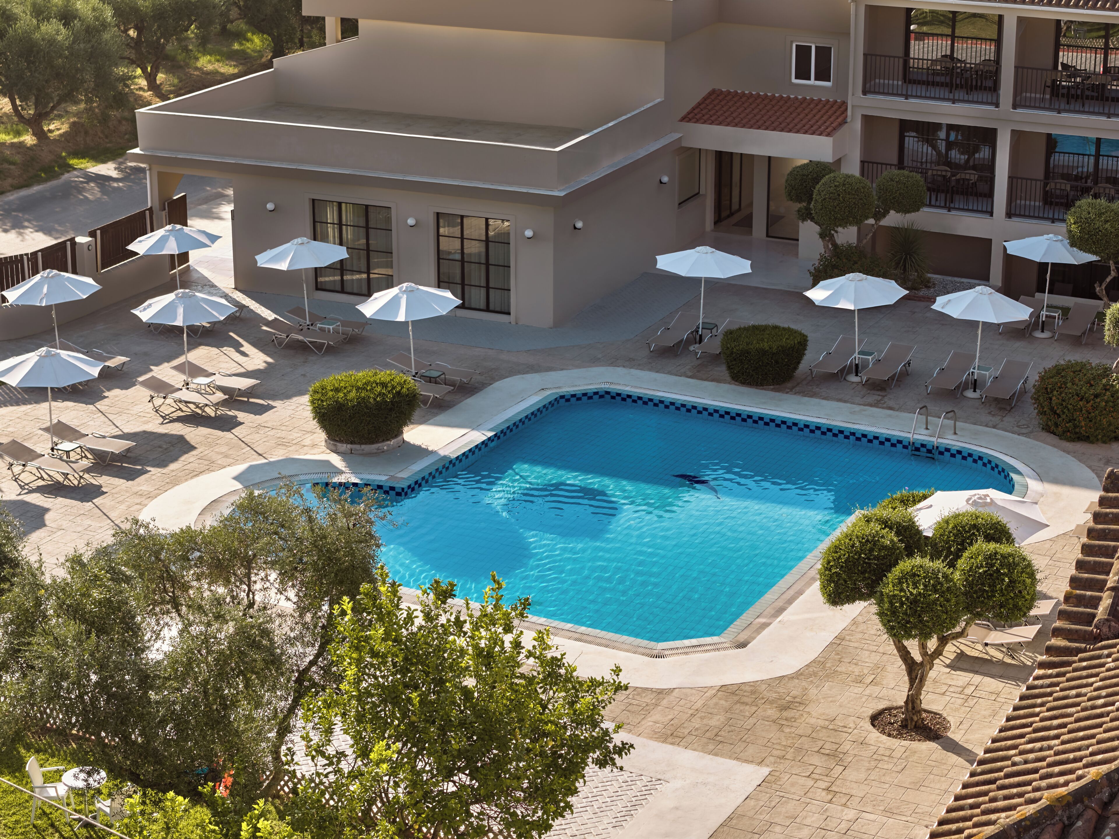 Ein Swimmingpool mit Liegestühlen und Sonnenschirmen, umgeben von einem Gebäude mit mehreren Etagen und Balkonen.