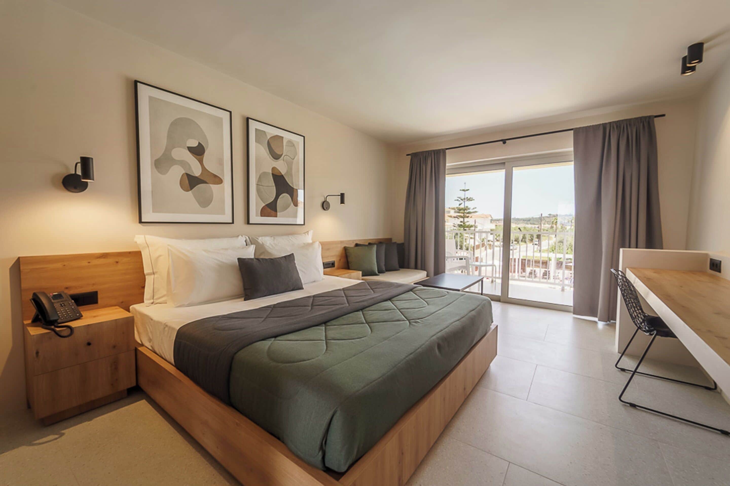 Una habitación de hotel moderna con una cama grande, un escritorio, un teléfono en la mesita de noche y obras de arte en las paredes.