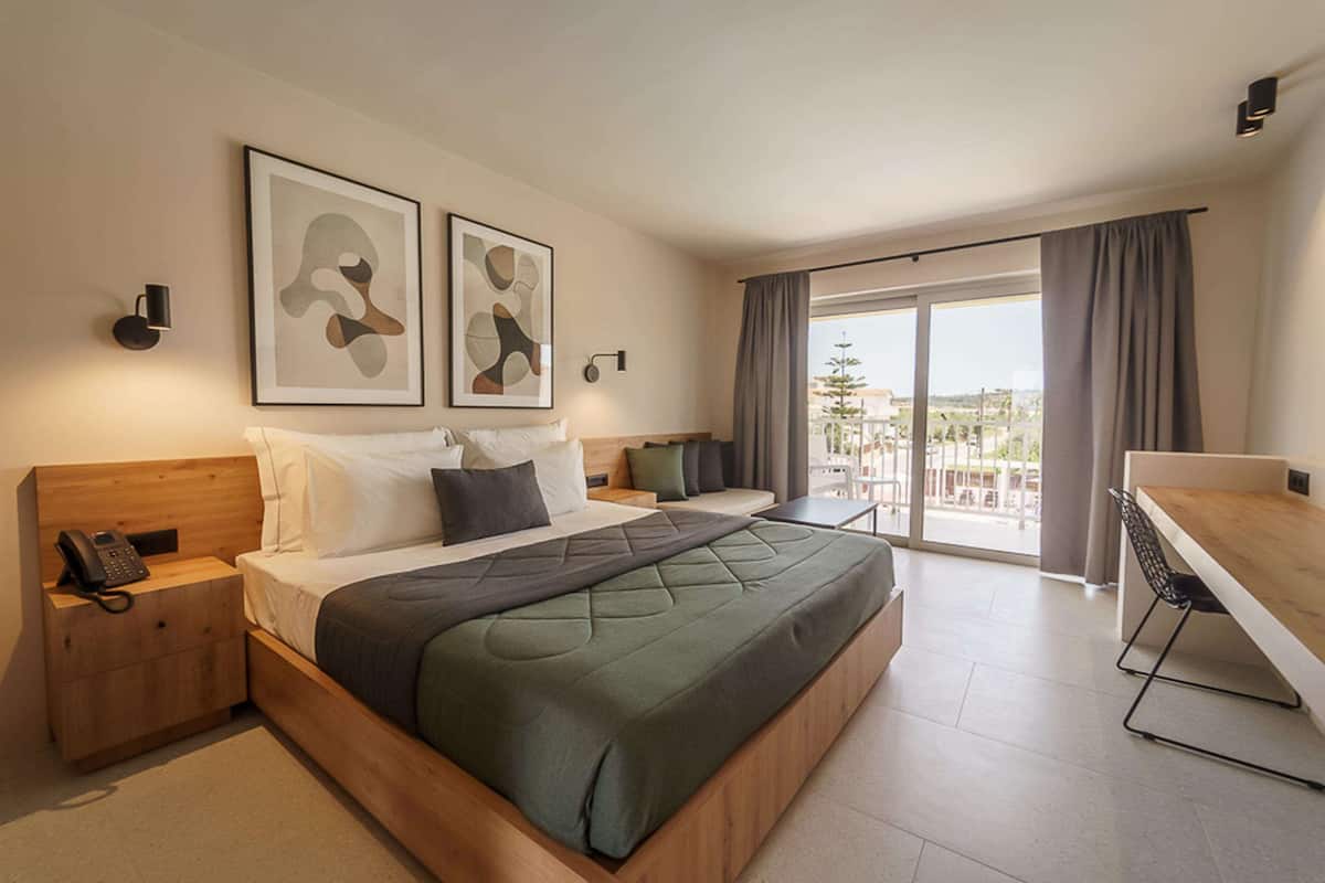 A modern hotel room with a large bed, a desk, and a balcony with a view.