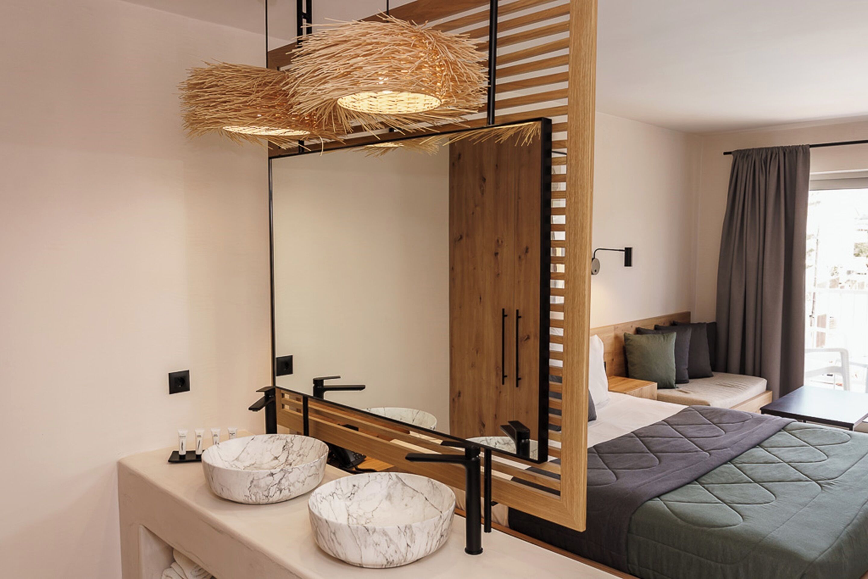 A modern hotel room with a large mirror, a wooden wardrobe, a bed with a green quilt, and a round marble sink.