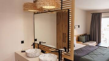 A modern hotel room with a large mirror, a wooden wardrobe, a bed with a green quilt, and a round marble sink.