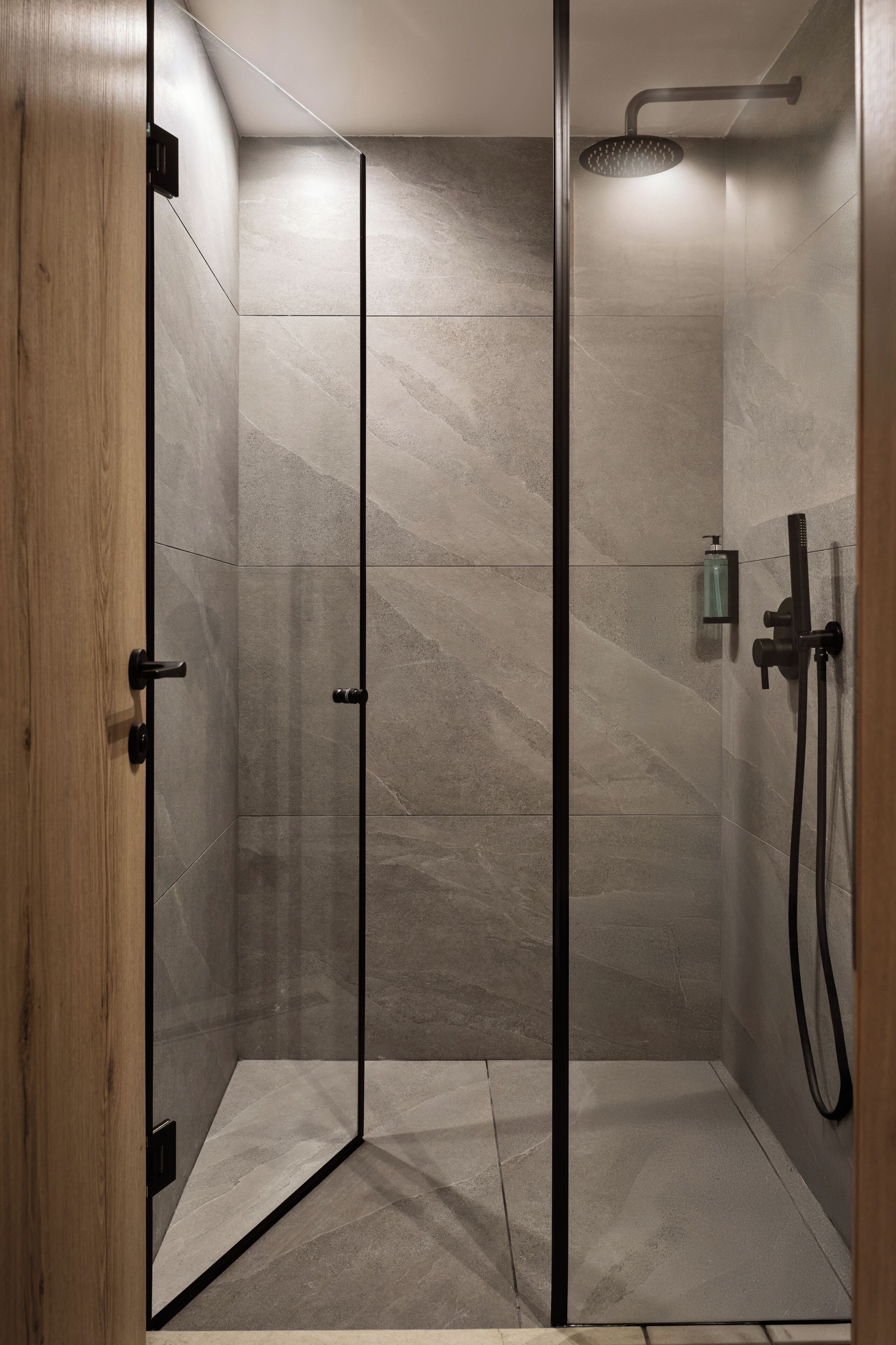 A modern shower with a glass door, a handheld showerhead, and a handheld shower attachment.