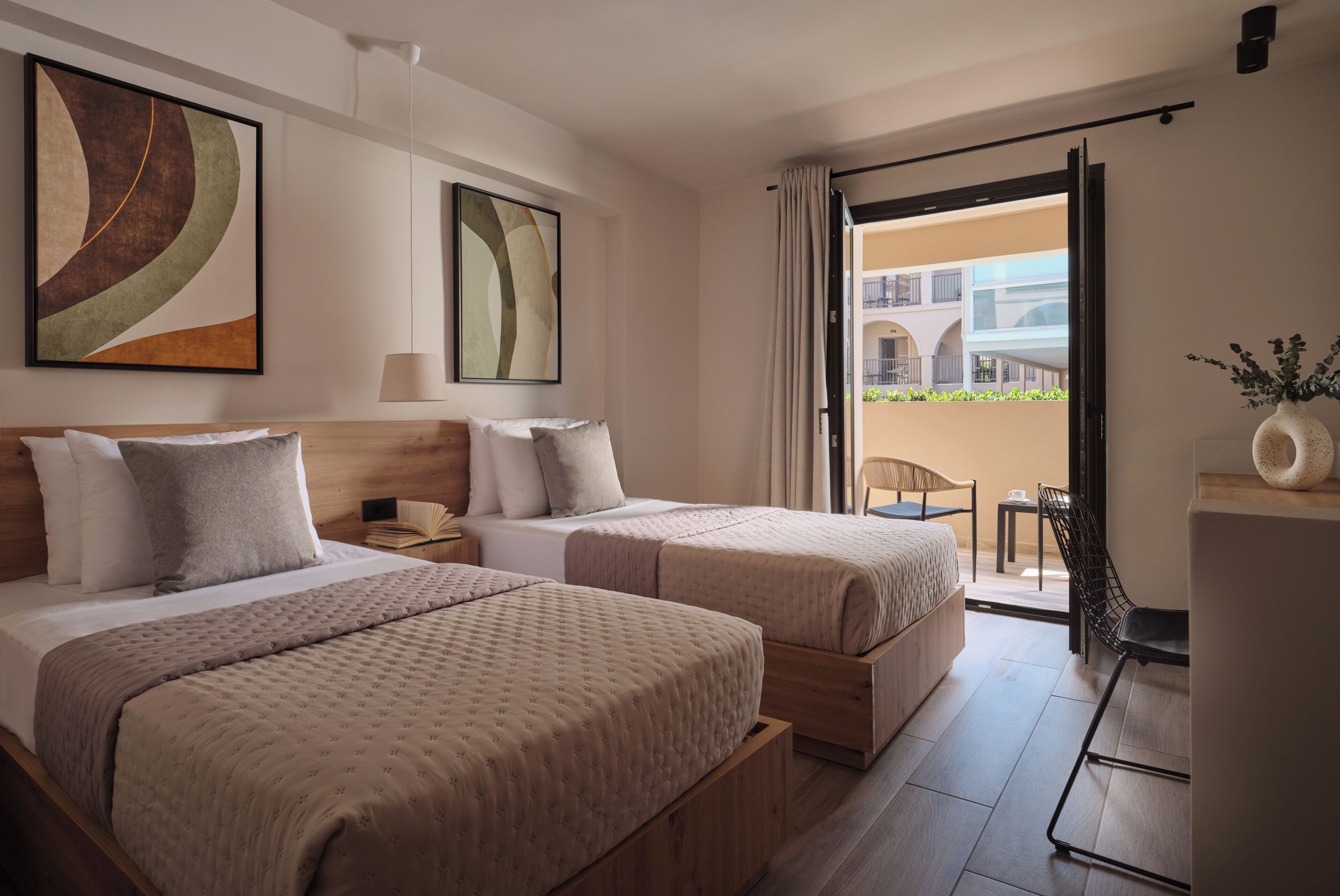 Habitación de hotel con dos camas, una mesita, una silla y vista al balcón exterior.