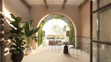 An outdoor patio with a round table and chairs, a large potted plant, and an arched entrance with greenery.