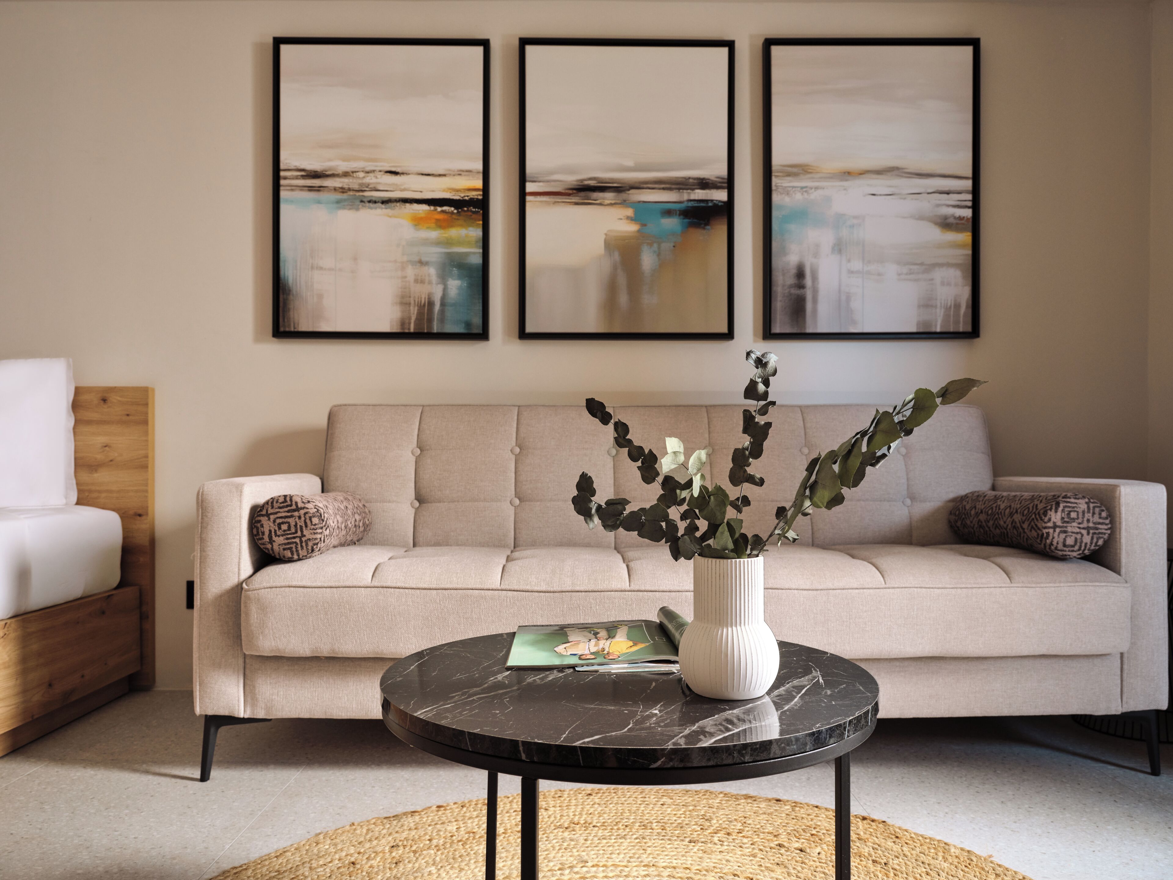 Un salón con un sofá, una mesa redonda con un florero y tres obras de arte enmarcadas en la pared.
