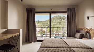 Habitación de hotel con cama, escritorio y silla. Balcón con vista a zonas verdes y edificios.