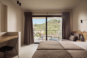 Camera d'albergo con un letto, una scrivania e una sedia. Include un balcone con vista su spazi verdi e edifici.