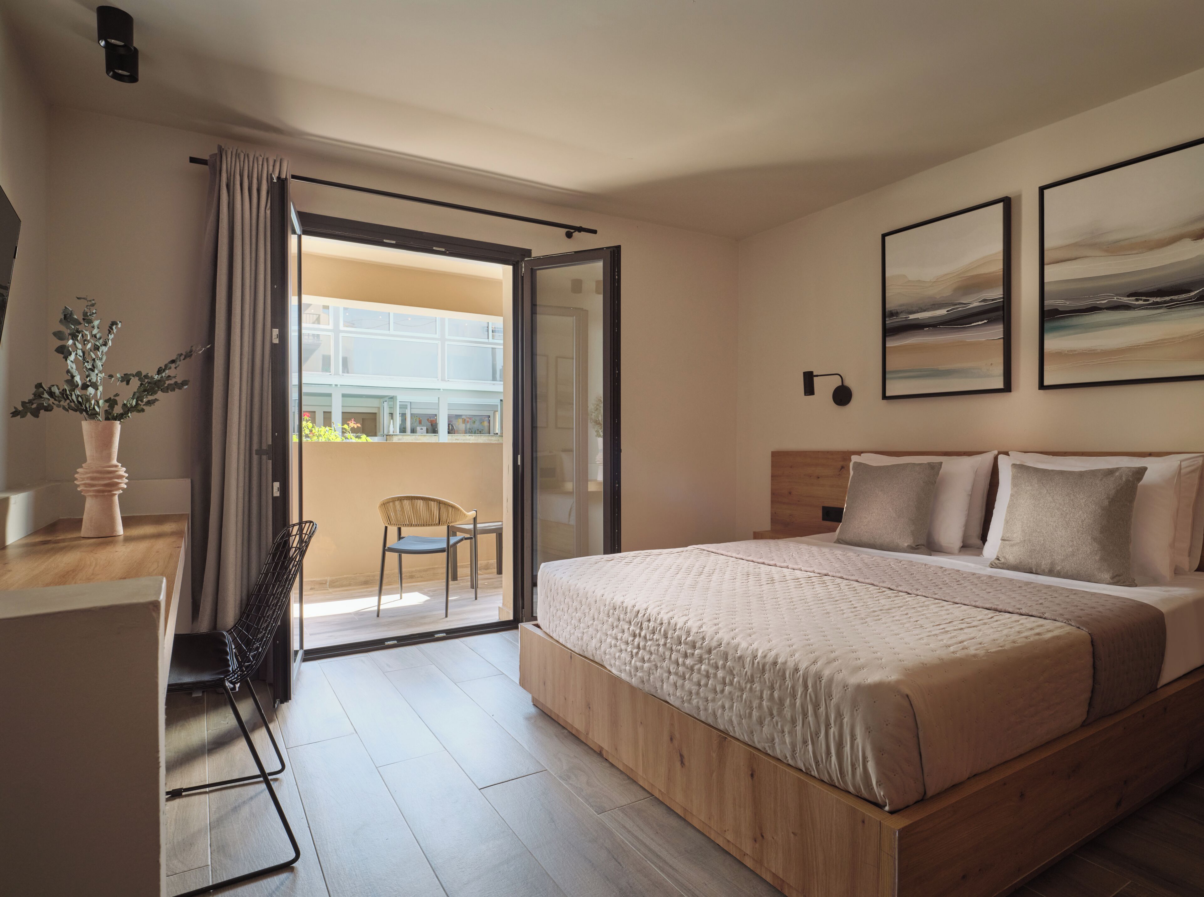 A hotel room with a bed, a chair, a table, a potted plant, and a balcony with a view.