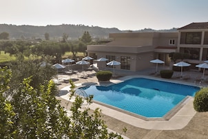 Una piscina con lettini e ombrelloni, immersa in un giardino curato e affiancata da un edificio con un balcone.