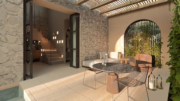 Una moderna terrazza esterna con un muro in pietra, un tavolo rotondo con sedie e una scala che conduce a un ambiente interno.
