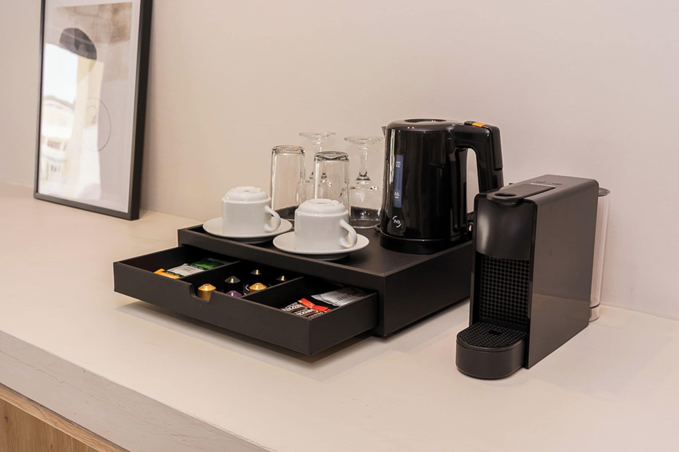 Un coin café équipé d’une machine à café, de tasses et d’un tiroir contenant des dosettes de café.