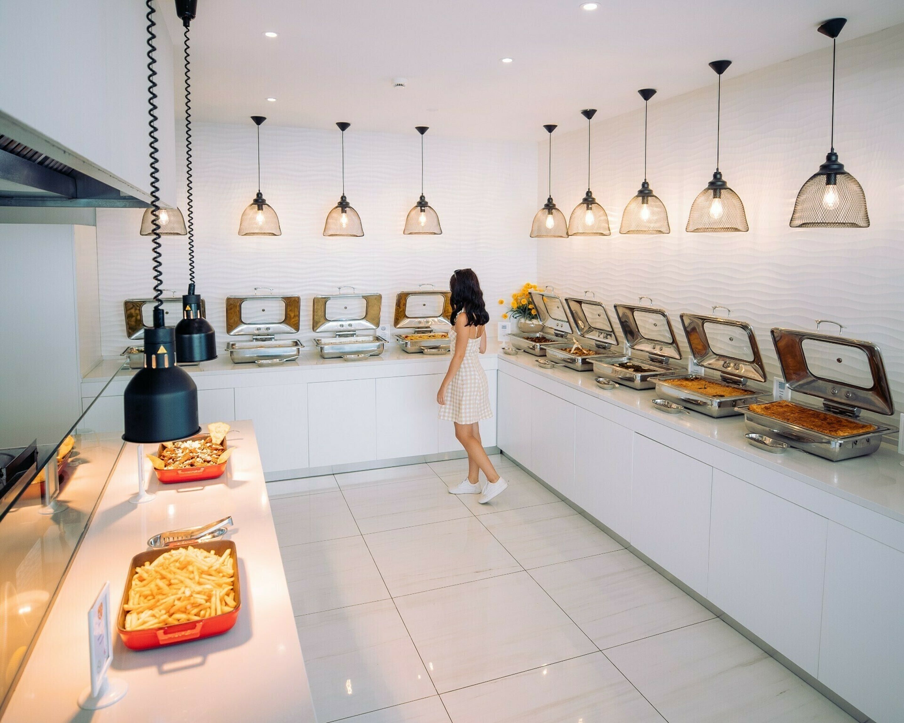 A buffet area with multiple food stations, a person serving, and pendant lighting.