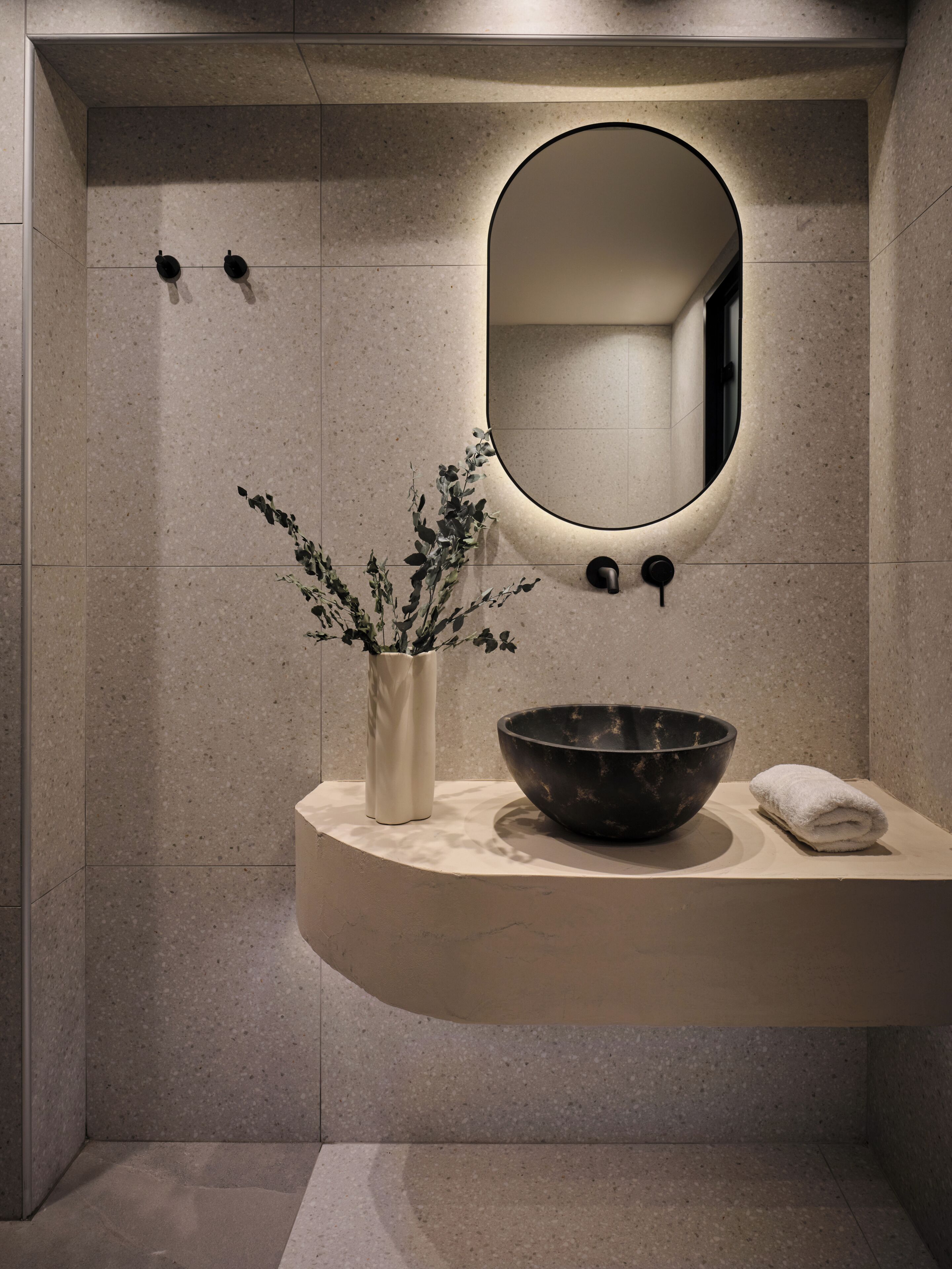 A bathroom with a curved vanity, a large mirror, a vase with plants, and a bowl.