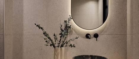 A bathroom with a curved vanity, a large mirror, a vase with plants, and a bowl.