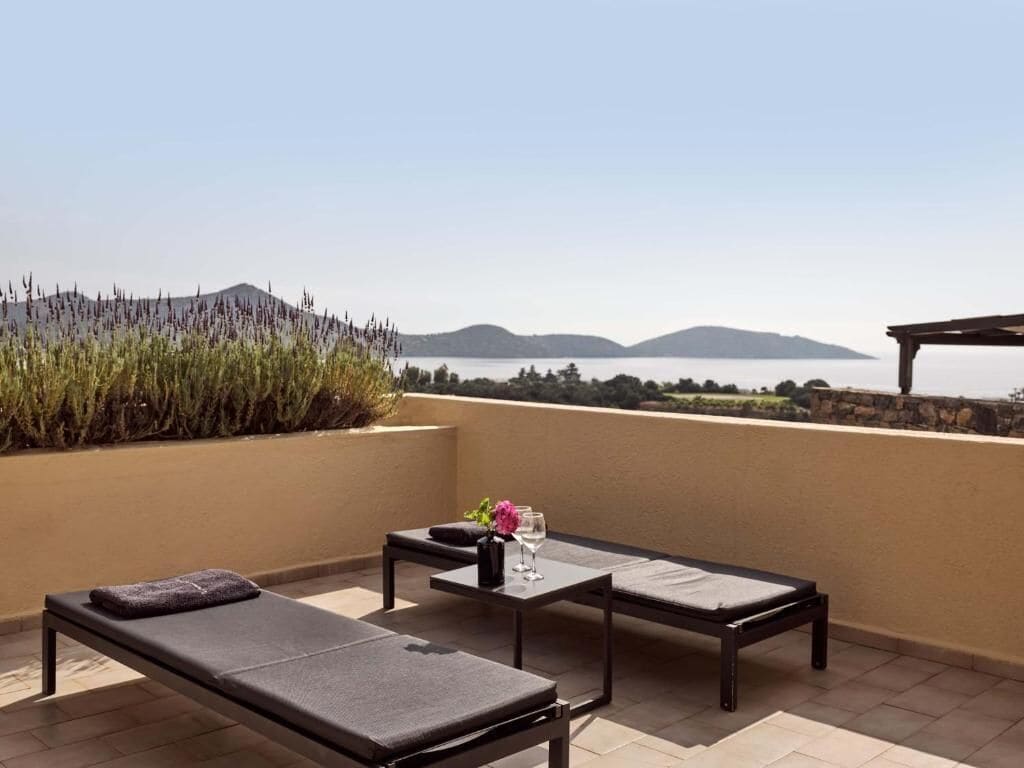 A terrace with two lounge chairs, a table, and a vase of flowers.