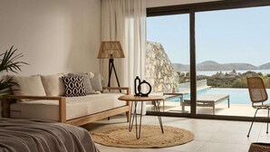 A modern bedroom with a large window, a bed, a sofa, a small round table, and a chair. - Elounda Palm Hotel (Agios Nikolaos)