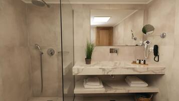 Un baño moderno con ducha de vidrio, lavamanos de mármol y un espejo con una pequeña planta.