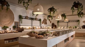 A modern kitchen with a central island, hanging plants, and a variety of kitchenware. - Elounda Palm Hotel (Agios Nikolaos)