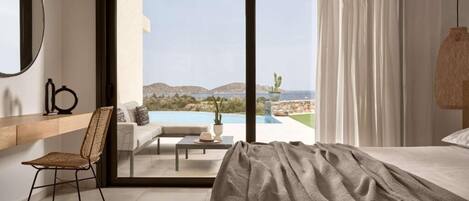 Un dormitorio con una cama grande, una silla, una mesita y vistas a una piscina y al paisaje a través de una puerta corrediza.
