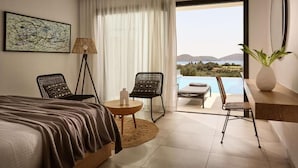 A modern hotel room with a bed, two chairs, a small table, and a view of the sea. - Elounda Palm Hotel (Agios Nikolaos)