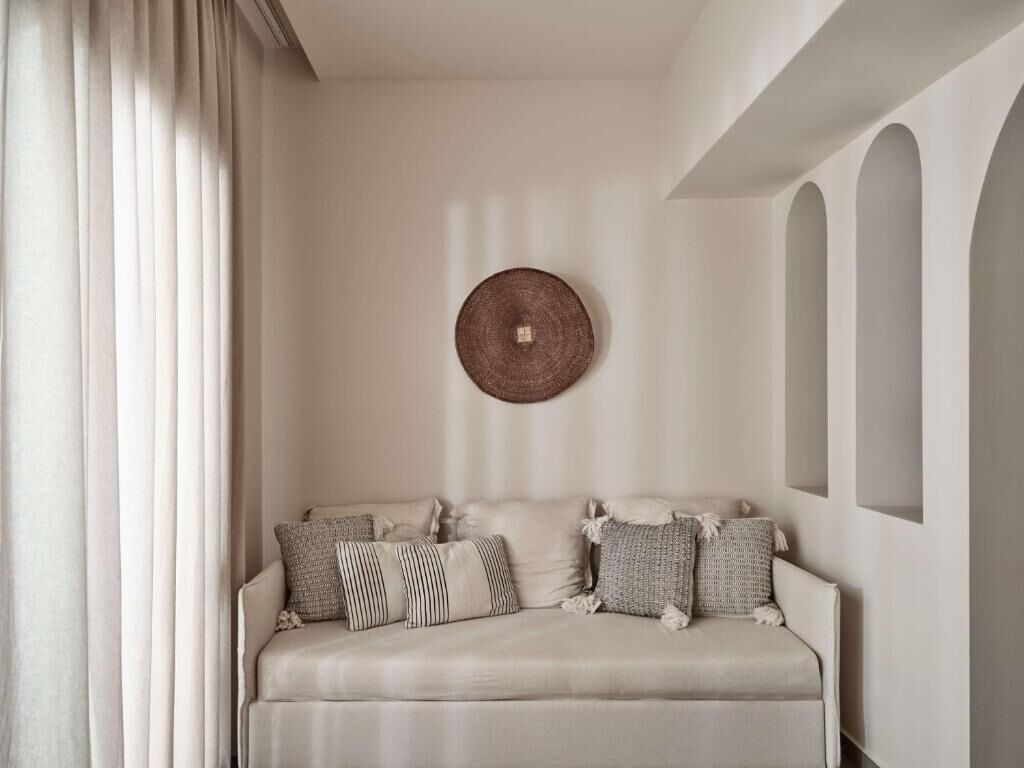 Un salón con tonos neutros, un sofá decorado con cojines estampados, una pieza de arte de pared trenzada y un ventanal con vistas al exterior.