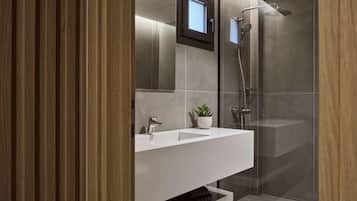 Un baño moderno con ducha de vidrio, tocador blanco con una planta y un espejo sobre el lavabo.