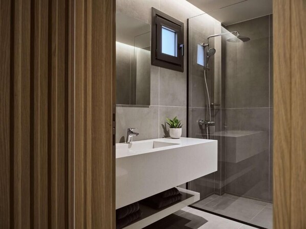 A modern bathroom with a glass-enclosed shower, a white vanity with a plant, and a mirror above the sink. - Elounda Palm Hotel (Agios Nikolaos)