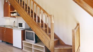 Une cuisine avec un escalier en bois, un four à micro-ondes, une télévision et un saladier de pommes sur une table.