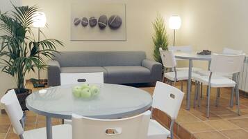 Un comedor moderno con una mesa redonda de cristal, sillas blancas, un sofá gris y una obra de arte colgada en la pared.