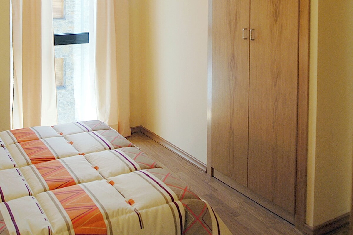 A bedroom with a bed, a wooden wardrobe, and a window with curtains.