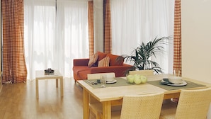 Ein Essbereich mit Holztisch, Korbstühlen, einem roten Sofa und einer Kübelpflanze.