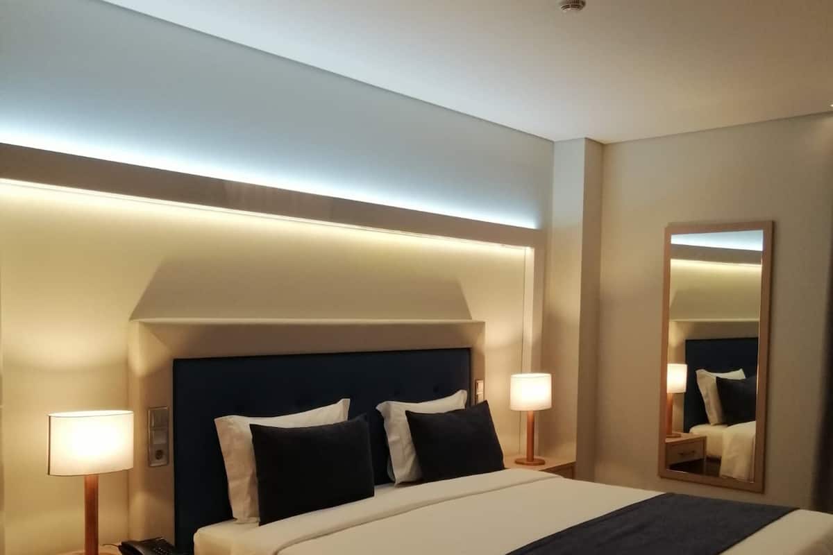 A modern hotel room with a large bed, bedside lamps, a nightstand, and a mirror.