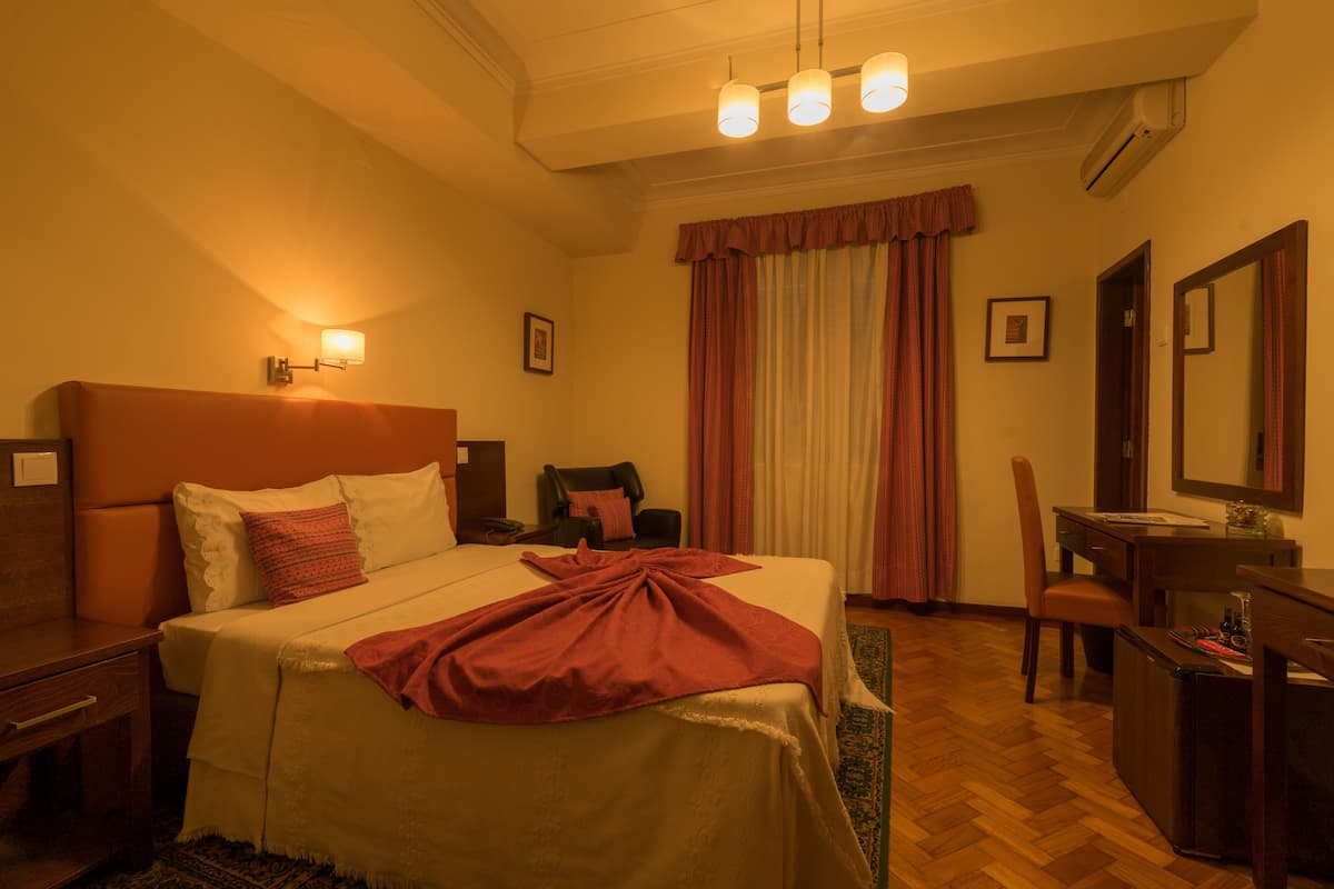 A hotel room with a bed, a desk, a chair, a mirror, and a window with curtains.
