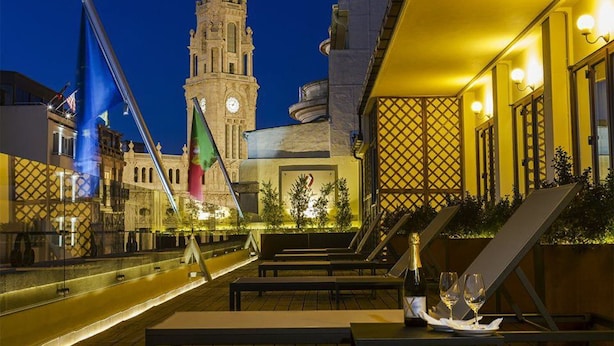A rooftop terrace with a view of a historic clock tower, outdoor seating, and a decorative fence. - Pão de Açúcar – Vintage Bumper Car Hotel (Porto)