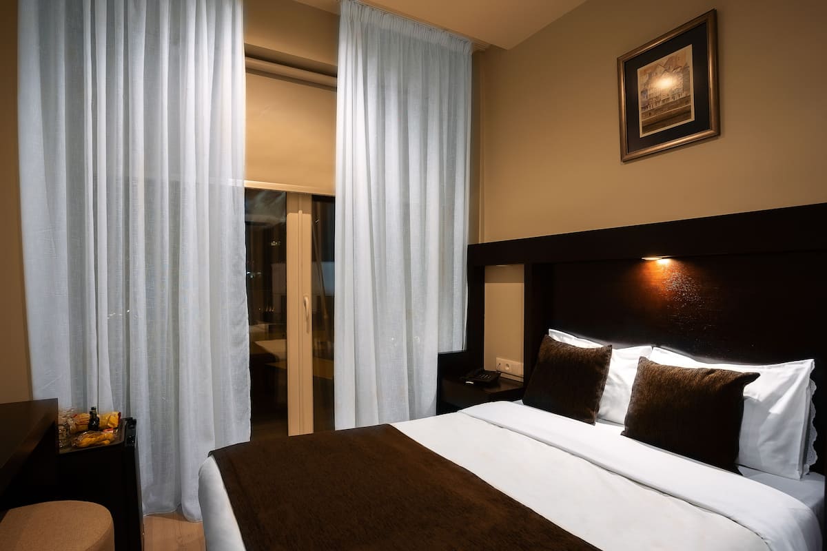A hotel room with a large bed, a nightstand, a desk, and a window with curtains.