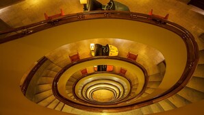 A grand spiral staircase with a central column and wooden handrails, surrounded by a polished stone floor. - Pão de Açúcar – Vintage Bumper Car Hotel (Porto)
