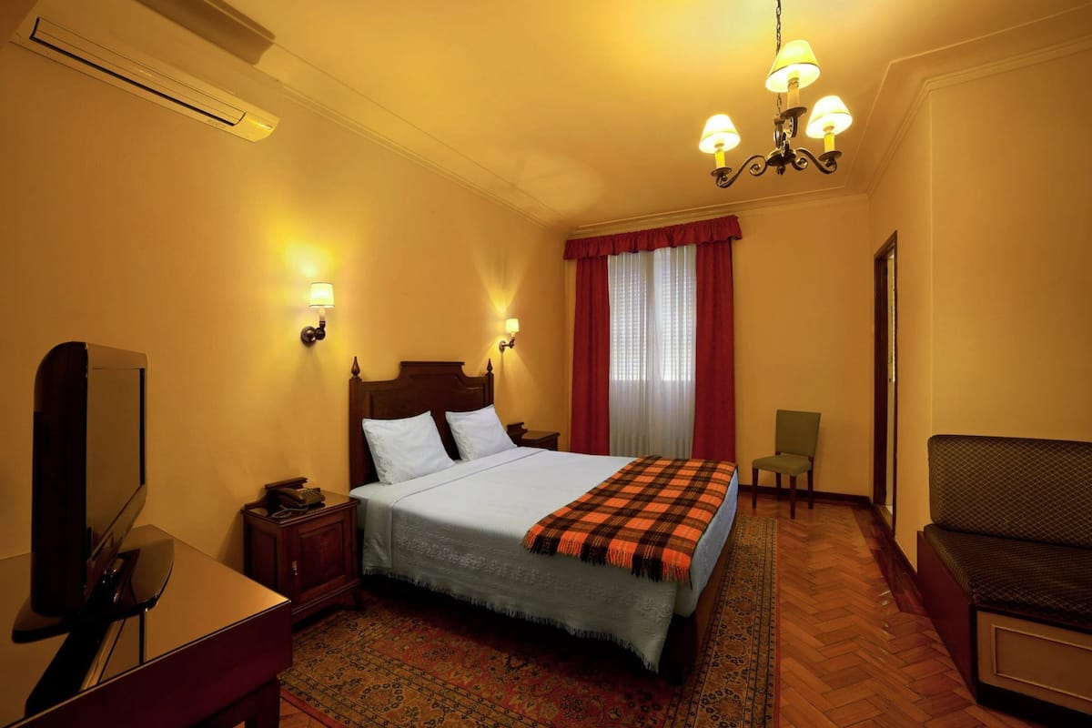 A hotel room with a bed, a desk with a mirror, a chair, and a sofa.
