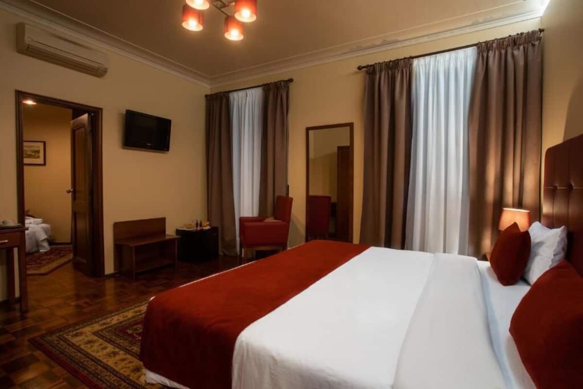 A hotel room with a large bed, a desk, a chair, a TV, and a mirror.