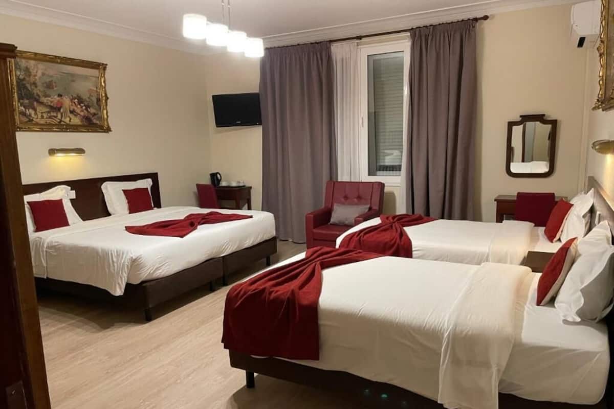 A hotel room with two beds, a red chair, a television, and a window with curtains.