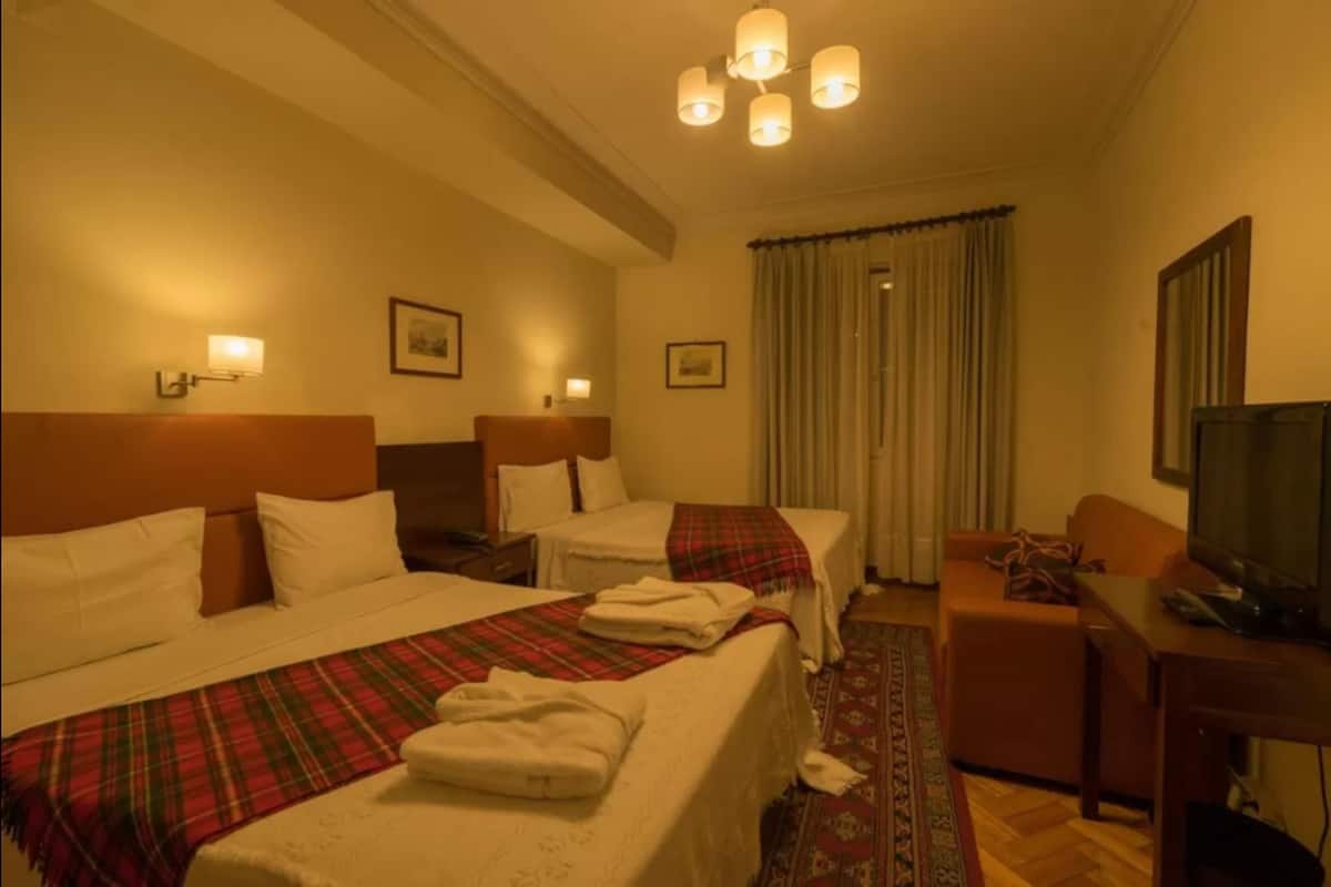 A hotel room with two beds, a desk, a television, and a window with curtains.