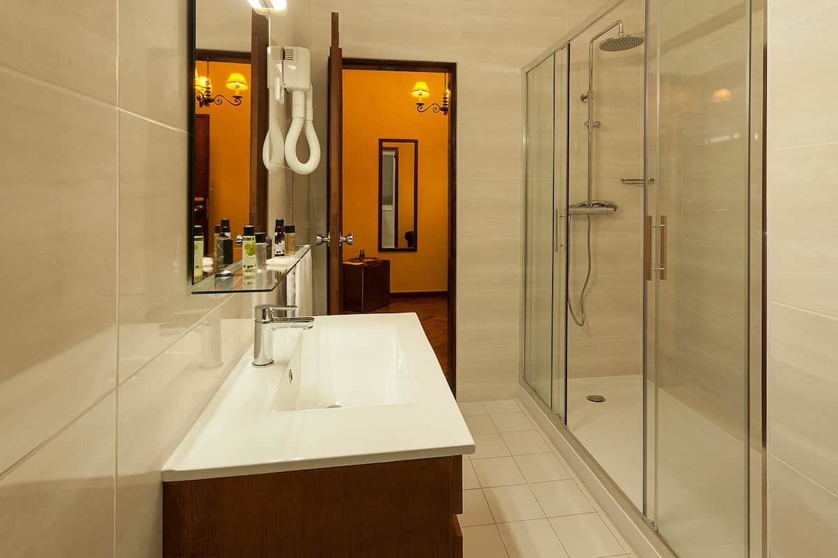 A modern bathroom with a large white sink, a glass shower enclosure, and a mirror with a hairdryer.