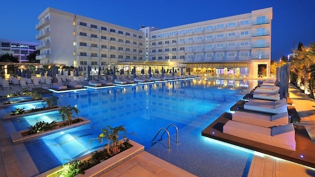 A hotel with a large swimming pool, multiple lounge areas, and a well-lit exterior. - Nestor Hotel (Ayia Napa)