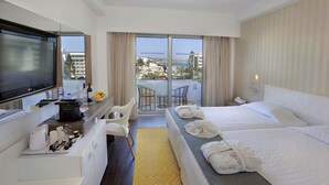 A hotel room with a bed, a desk with a TV, a small table with chairs, and a view of the sea. - Nestor Hotel (Ayia Napa)