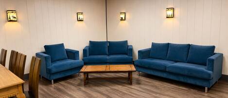 A room with two blue sofas, a wooden coffee table, and a dining table with chairs.