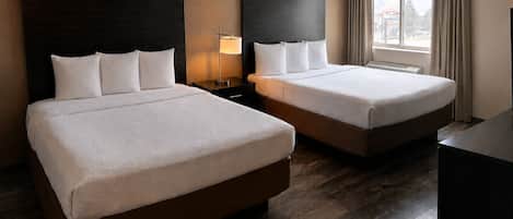 A hotel room with two beds, a nightstand with a lamp, a window with curtains, and a view of the outside.