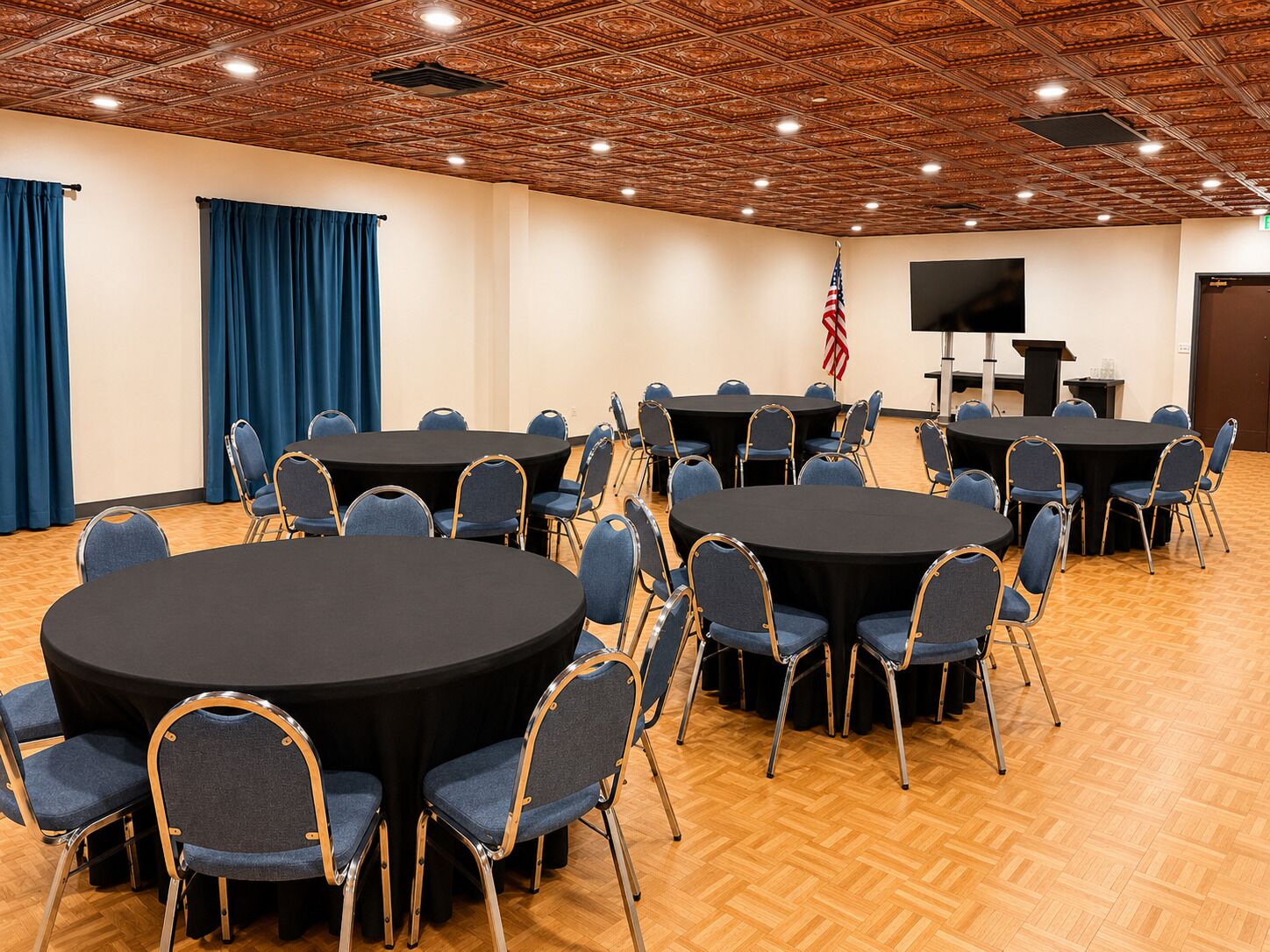 Ein Konferenzraum mit runden Tischen und Stühlen, einer Holzbalkendecke und der amerikanischen Flagge.