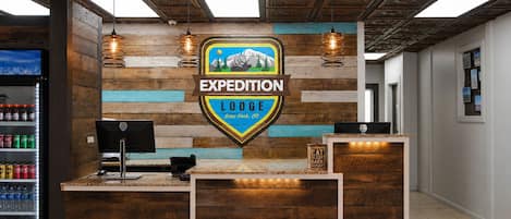 Ein Empfangsschalter mit Holztapete, ein Logo für 'Expedition Lodge' und ein Wandschild mit einer Berglandschaft.